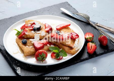 Köstliche traditionelle Crepes mit Schlagsahne und frischen Erdbeeren auf grauem Hintergrund. Leckere Crepes, dünne Pfannkuchen. Leckeres Frühstück. Draufsicht, Stockfoto