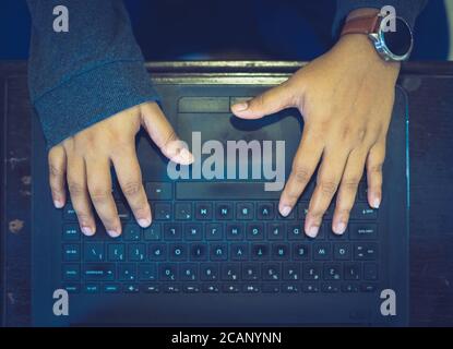 Nahaufnahme der Hände einer Frau, die von zu Hause aus mit einem weißen Laptop und einer Smartwatch in der Hand arbeitet, mit verschwommenem Hintergrund. Stockfoto