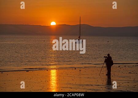 Murmbles, Swansea, Großbritannien. August 2020. Ein Mann fotografiert den Sonnenaufgang vom Strand vor dem Parkplatz Knab Rock im kleinen Dorf Mumbles bei Swansea am frühen Morgen. Quelle: Phil Rees/Alamy Live News Stockfoto