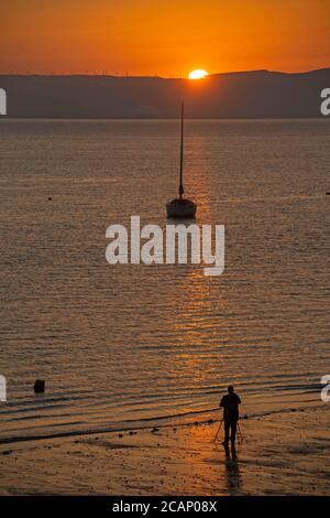 Murmbles, Swansea, Großbritannien. August 2020. Ein Mann fotografiert den Sonnenaufgang vom Strand vor dem Parkplatz Knab Rock im kleinen Dorf Mumbles bei Swansea am frühen Morgen. Quelle: Phil Rees/Alamy Live News Stockfoto