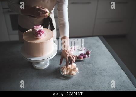 Frau, die Kuchen dekorieren mit Blumenrosen Aufenthalt auf Küchentisch Nahaufnahme zu Hause. Hochzeitstag. Selektiver Fokus. Stockfoto