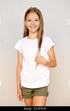 Portrait von positiven Teenager-Mädchen stehen mit gekreuzten Beinen und berühren Haare Stockfoto