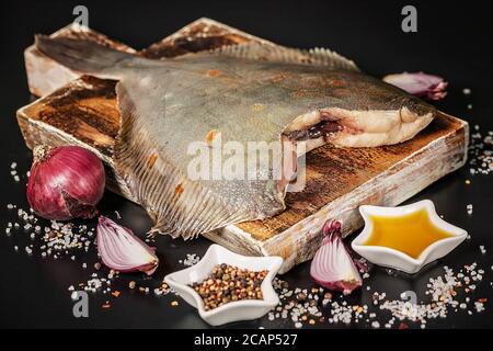 Steinbutt Flunder auf einem hölzernen Schneidebrett auf einem dunklen Hintergrund. Rote Zwiebel, Salz, Pfeffer und Gewürze Stockfoto