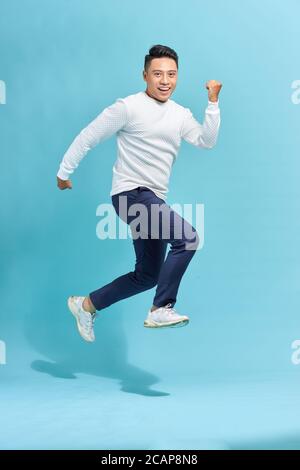 Bild von fröhlichen jungen Mann in schwarzem T-Shirt gekleidet Springen über blauen Hintergrund machen Sieger Geste. Stockfoto