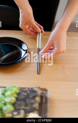 Frauenhände arrangieren den Tisch mit verschiedenen Sushi-Sets auf einem Holztisch in einem sonnigen Zuhause Stockfoto