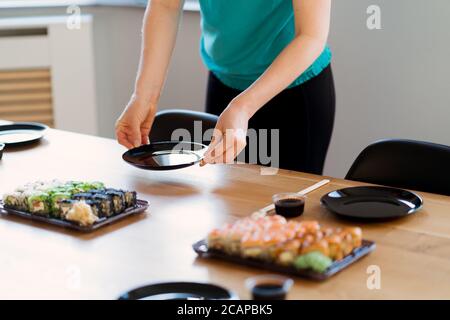 Frauenhände arrangieren den Tisch mit verschiedenen Sushi-Sets auf einem Holztisch in einem sonnigen Zuhause Stockfoto