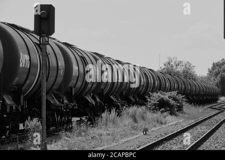 Magdeburg, 27. Juni 2020: Langer Zug mit Kesselwagen hintereinander auf einer Spur neben leeren Schienen, schwarz-weiß Stockfoto