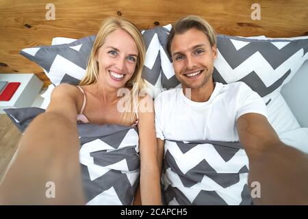 Junges Paar unter Selfie im Bett - glücklich Liebhaber mit Es macht Spaß, selbst Fotos zu machen, die auf dem Bett unter den Decken liegen Zu Hause Stockfoto