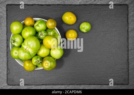 Grüne Tomaten in einem Emaille-Sieb auf Schieferplatte mit Speicherplatz kopieren Stockfoto