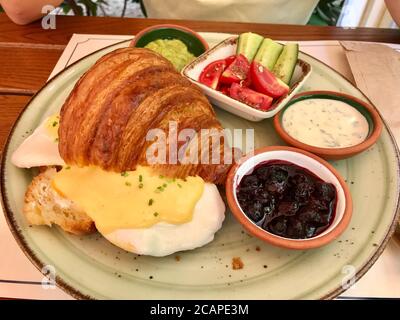 Pochierte Eier mit Croissant-Sandwich und Sauce Hollandaise serviert mit Marmelade, Joghurt im Restaurant. Stockfoto