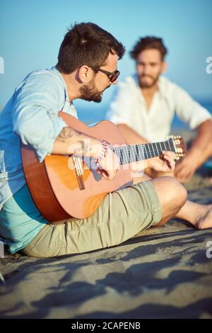 Jungs, die am Strand rumhängen und Gitarre spielen Stockfoto