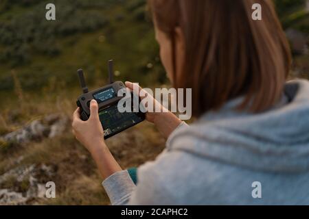 Junge kaukasische Frau, die eine fliegende Drohne mit Fernbedienung steuert Mit einer malerischen Landschaft im Hintergrund Stockfoto