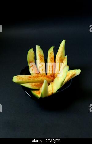 Frische grüne Mango mit gemischtem Salz und gemahlenem Chilipulver Auf schwarzem Hintergrund Stockfoto