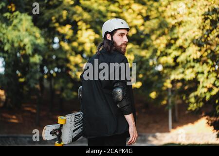 Der Mann mit dem Brett geht die Straße hinunter. Longboarding bei Sonnenuntergang. Stockfoto