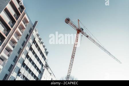 Schräge diagonale Ansicht vom Boden einer hohen Konstruktion Kran in einem Wohnviertel in der Nähe eines Wohnhauses mit Klarer blauer Himmel im Hintergrund Stockfoto