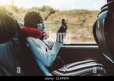 Seitenansicht einer schwarzen Touristenfrau mit einem Smartphone auf einem Sitz eines modernen Linienbusses in der Nähe des Fensters hat sie ein rotes Luftkissen am Hals Stockfoto