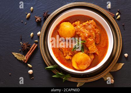 Asiatisches Speisekonzept hausgemachte würzige Chicken Masala oder Thai Massaman Curry mit Gewürzen im Vordergrund auf schwarzem Schieferstein mit Kopie Platz Stockfoto