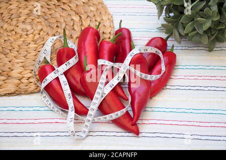 Rote Paprika mit Maßband, Rushmat und dekorative Pflanze auf gemusterter Tischdecke. Diät-Konzept. Art und Weise der Gewichtsreduktion und Kalorienkontrolle. Stockfoto