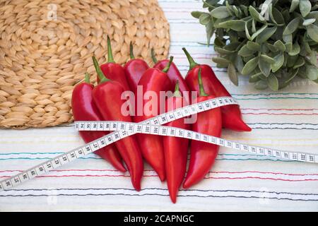 Rote Paprika mit Maßband, Rushmat und dekorative Pflanze auf gemusterter Tischdecke. Diät-Konzept. Art und Weise der Gewichtsreduktion und Kalorienkontrolle. Stockfoto