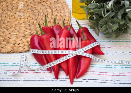 Rote Paprika mit Maßband, Rushmat und dekorative Pflanze, Olivenöl auf gemusterter Tischdecke. Diät-Konzept. Art und Weise, Gewicht und Kalorien zu verlieren. Stockfoto