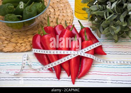 Rote und grüne Paprika mit Maßband, Rushmat und dekorative Pflanze, Olivenöl auf gemusterter Tischdecke. Diät-Konzept. Art und Weise der Gewichtsreduktion. Stockfoto