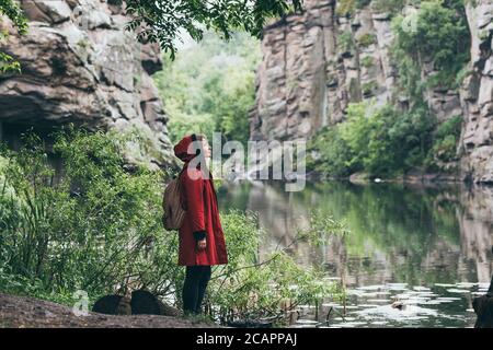 Frau in rotem Mantel neben Steinmauer der Klippe in Buky Canyon, Ukraine Stockfoto