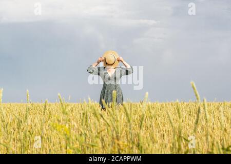 Frau im Strohhut zu Fuß durch das Roggenfeld am Sommertag. Versteckt Gesicht hinter ihrem runden Hut. Stockfoto