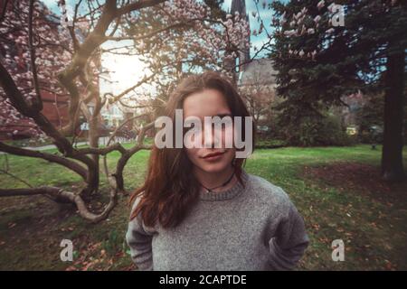 Porträt einer jungen, lächelnden Frau in einem Park vor einem Magnolienbaum Stockfoto