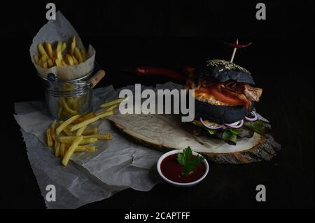 Schwarzer Burger auf einem Holzbrett und Pommes mit Tomate Soße Stockfoto