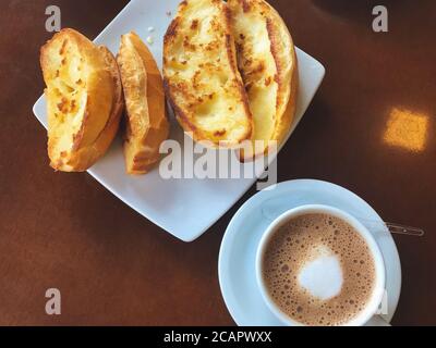 Brasilianisches Frühstück. Cappuccino Tasse und geröstetes Brot mit Butter Hintergrund Stockfoto