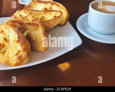 Brasilianisches Frühstück. Cappuccino Tasse und geröstetes Brot mit Butter Hintergrund Stockfoto