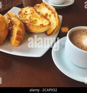 Brasilianisches Frühstück. Cappuccino Tasse und geröstetes Brot mit Butter Hintergrund Stockfoto