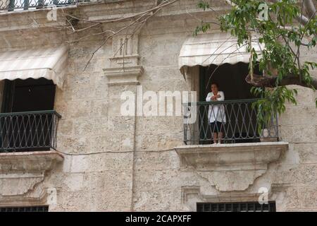 Frau, die vom Balkon aus auf das Haus im Kolonialstil blickt, Havanna, Kuba Stockfoto