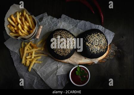 Schwarze Burger-Brötchen mit Sesambrötchen in einem Eimer Ein dunkler Hintergrund Stockfoto