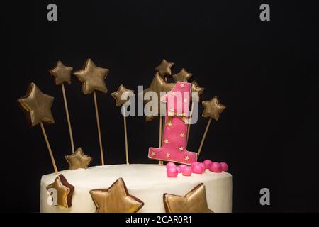 Geburtstagskuchen mit rosa Zahl 1 und goldenen Sternen verziert Von Lebkuchen auf einem dunklen Hintergrund Stockfoto