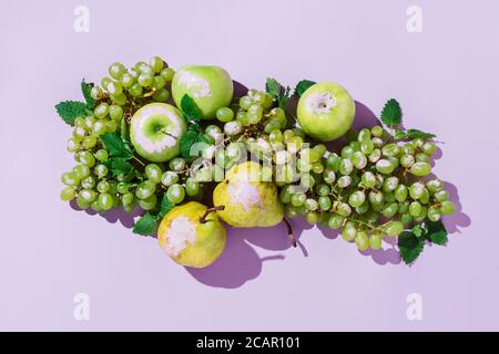 Frische grüne Trauben, Äpfel, Birnen und Kräuterblätter mit violetter Farbe auf buntem Hintergrund bemalt Stockfoto