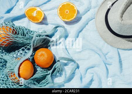 Picknick-Flatlay von Orangen in einer Öko-Saite und hut auf blauer Decke Stockfoto