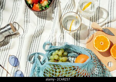 Sommer Picknick-Flatlay, Früchte, Beeren und Zitronenwasser auf gestreifter Baumwolldecke Stockfoto