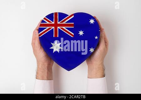 Flagge Australiens auf einer herzförmigen Schachtel in einer männlichen Hand. Weißer Hintergrund Stockfoto