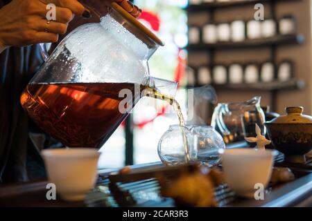 Traditionelle Chinesische Teezeremonie. Schwarzer oder roter Tee Gießen aus Glas große Teekanne in Glas Chahai auf dunklen Holztisch Hintergrund Stockfoto