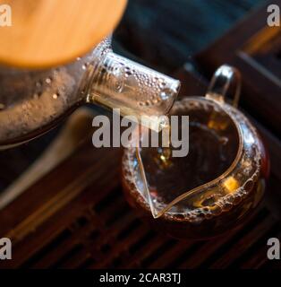 Traditionelle Chinesische Teezeremonie. Schwarzer oder roter Tee Gießen aus Glas große Teekanne in Glas Chahai auf dunklen Holztisch Hintergrund Stockfoto