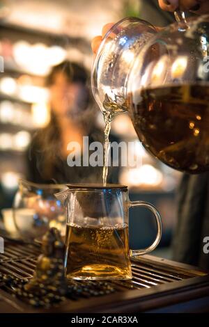 Traditionelle Chinesische Teezeremonie. Schwarzer oder roter Tee Gießen aus Glas große Teekanne in Glas Chahai auf dunklen Holztisch Hintergrund Stockfoto