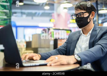 Asiatische Geschäftsleute sprechen am Telefon und mit Note Buch für die Arbeit, er trägt Maske zum Schutz Coronavirus Stockfoto
