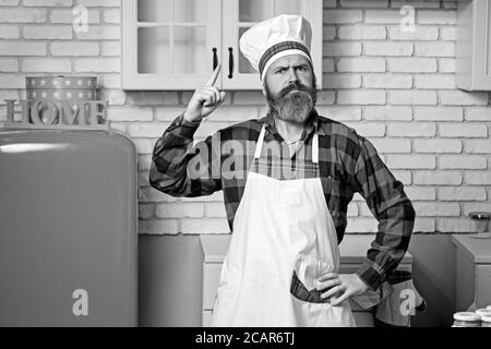 Junger lächelnder Koch in weißer Uniform und Hut im Inneren der modernen Restaurantküche. Bereit zum Essen. Stockfoto