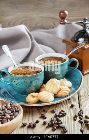 Zwei blaue Tassen schwarzen Kaffee, Kekse und Kaffeemühle umgeben von Leinentuch, Zuckerstückchen und Kaffeebohnen auf altem Holztisch Stockfoto