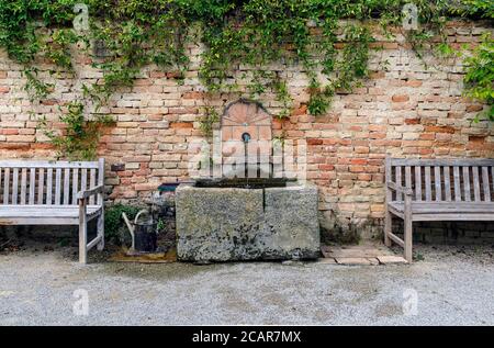 Wandbrunnen mit Steintrog zwischen zwei hölzernen Sofas vorher Eine alte Backsteinmauer in Österreich Stockfoto