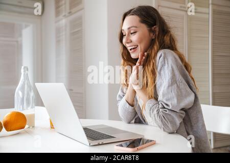 Portrait von Ingwer aufgeregt Frau zum Ausdruck Überraschung während der Arbeit mit Laptop in heller Küche Stockfoto