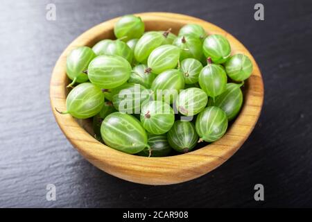 Frische Stachelbeeren in Holzschale auf schwarzem Stein Schiefer Hintergrund. Draufsicht. Stockfoto