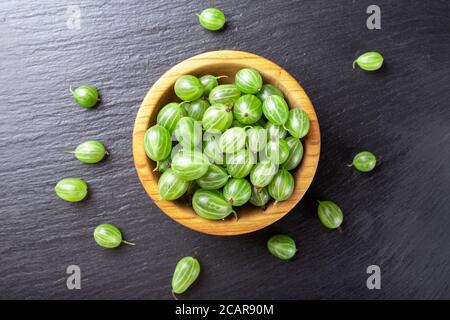 Frische Stachelbeeren in Holzschale auf schwarzem Stein Schiefer Hintergrund. Draufsicht. Stockfoto