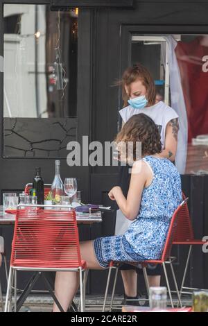 Clapham wartet auf Tische mit einer Gesichtsmask an der Northcote Road und ist nun für Autos gesperrt und öffnet an einem heißen Sommertag die Straße für Restaurants und Bars. Stockfoto